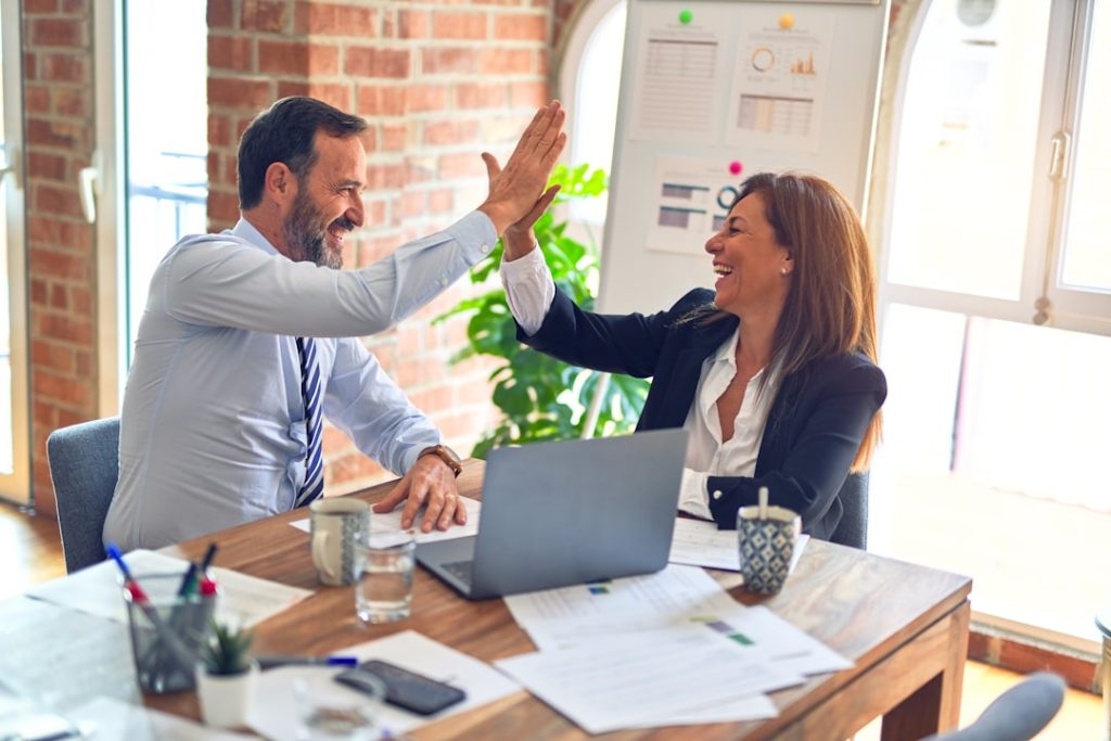 man-in-white-dress-shirt-sitting-beside-woman-in-black-long-sleeve-shirt-376kn-isple Two middle age business workers smiling happy and confident. Working together with smile on face hand giving high five at the office